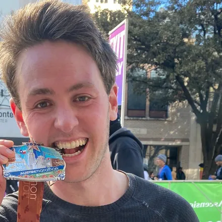 Richard Joseph Spinelli at the 2024 Austin Marathon finish, holding his medal up beside his face